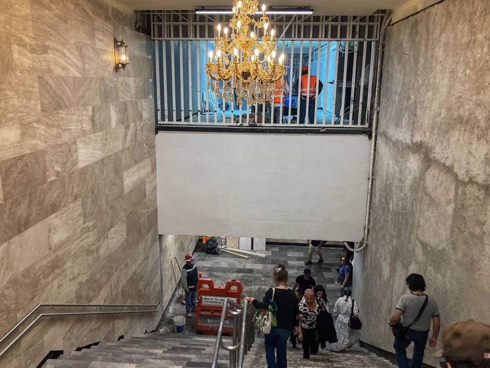 People descend stone stairs under a chandelier in a rustic corridor.