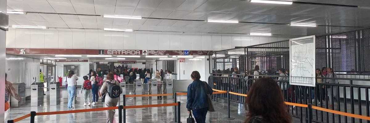 People entering a subway station through turnstiles, with orange barriers guiding the flow.