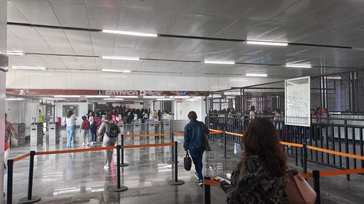 People entering a subway station through turnstiles, with orange barriers guiding the flow.