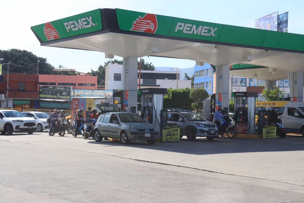 People fueling vehicles at a busy Pemex gas station under clear skies.