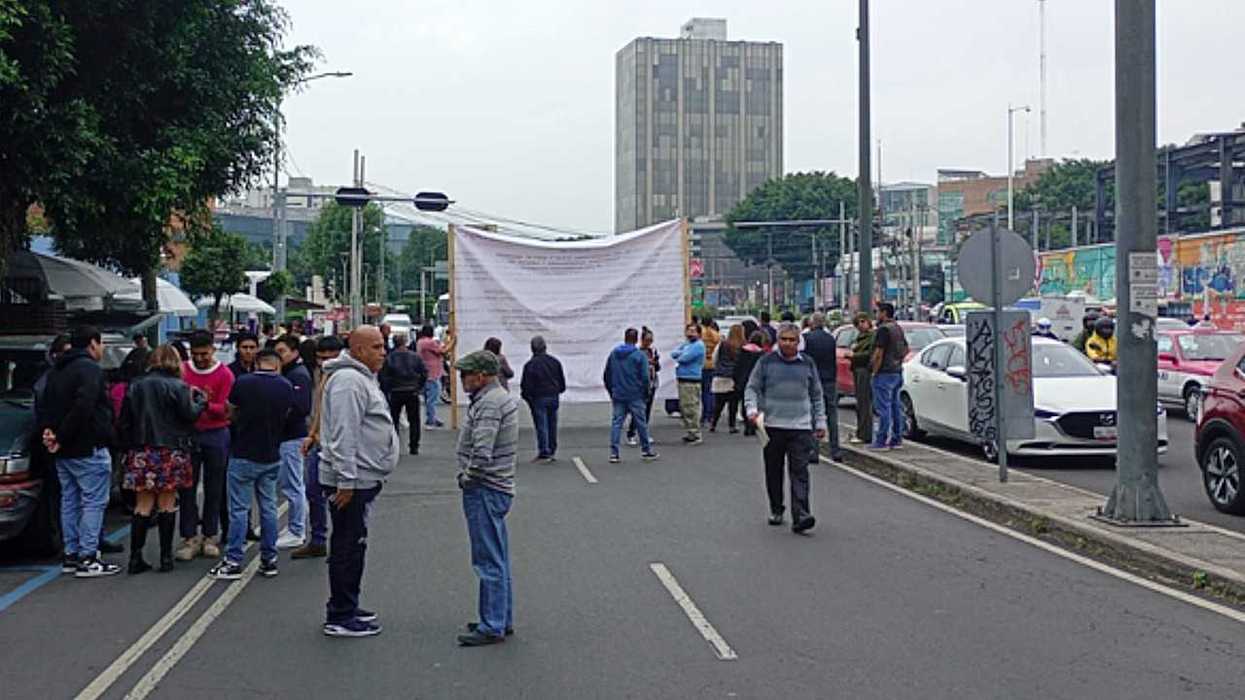 People gather on a street for a demonstration with a large banner in the background.