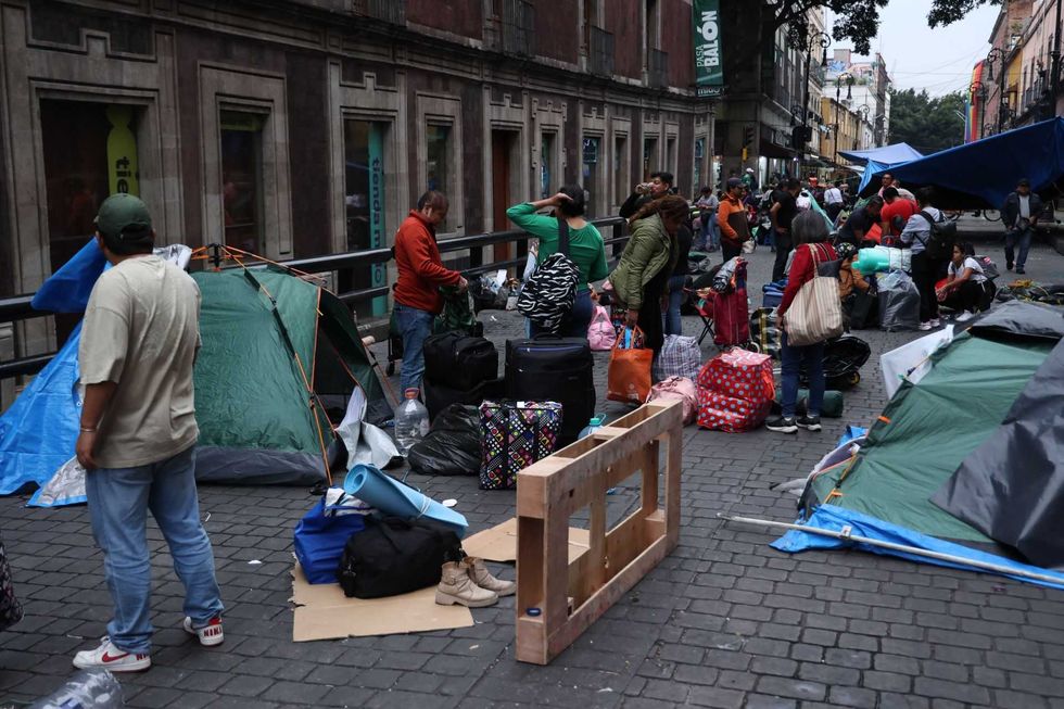 People gathered on a city street with tents and luggage, surrounded by buildings.