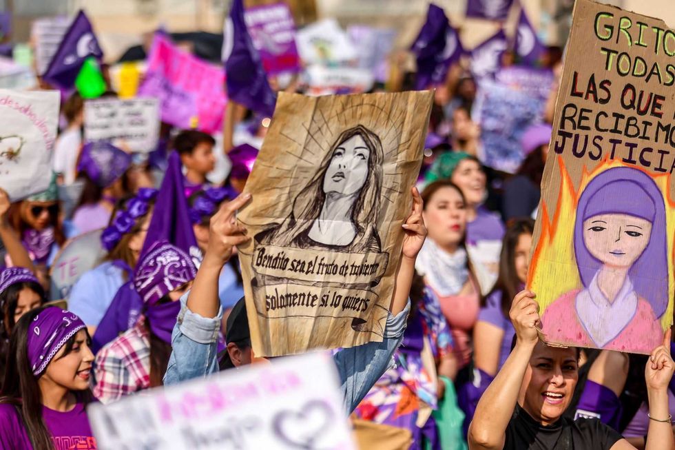 People holding signs and wearing purple at a women's rights protest.