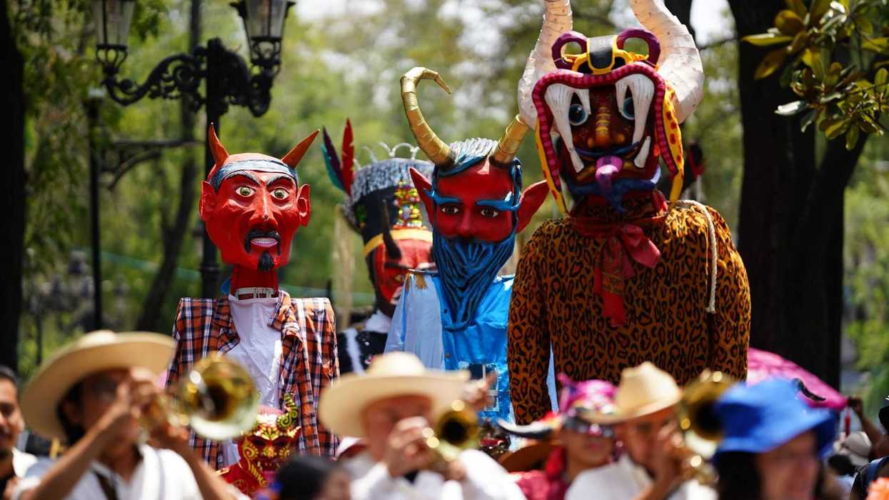 People in horned costumes and masks parade with musicians outdoors.