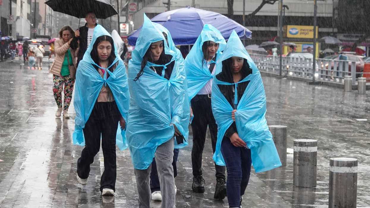 People in plastic ponchos walking in heavy rain on a city street.