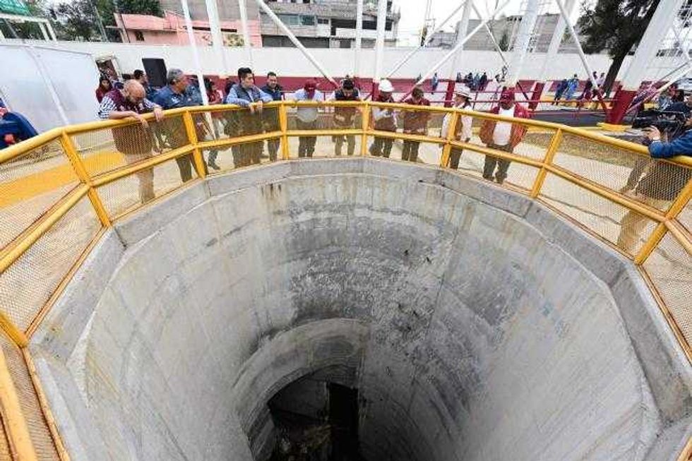 People observing a large circular construction pit with a yellow safety railing.