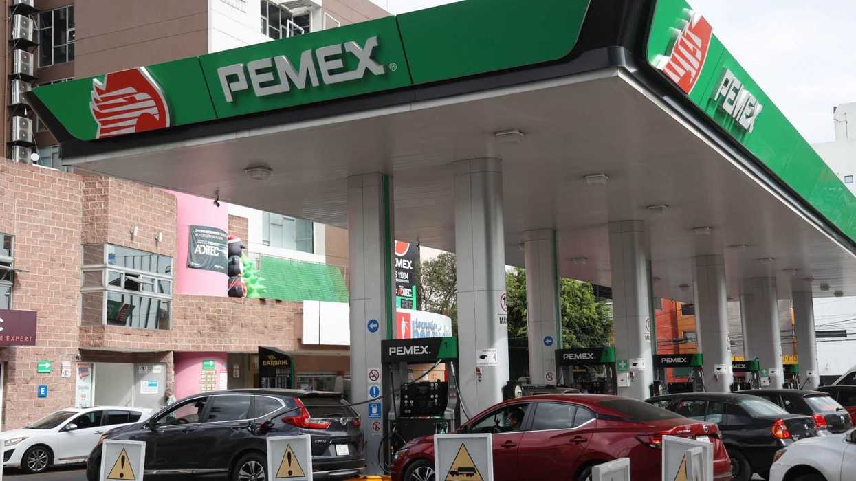 People refueling cars at a Pemex gas station with caution signs displayed.