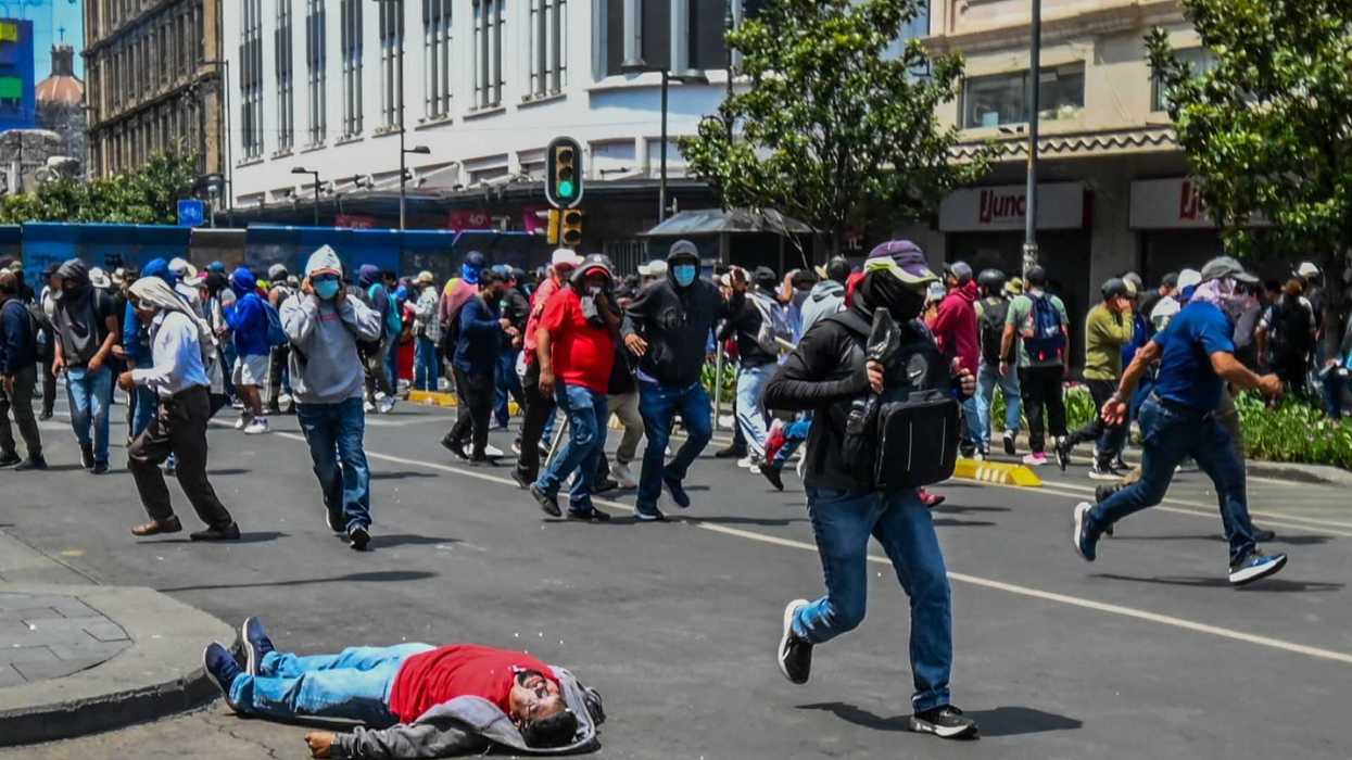 People run in a street protest, one person lies on the ground.