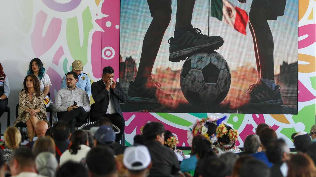 People seated at an event with a screen showing a soccer image.