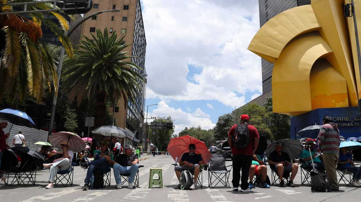 People sitting with umbrellas on a city street, large yellow sculpture in background.