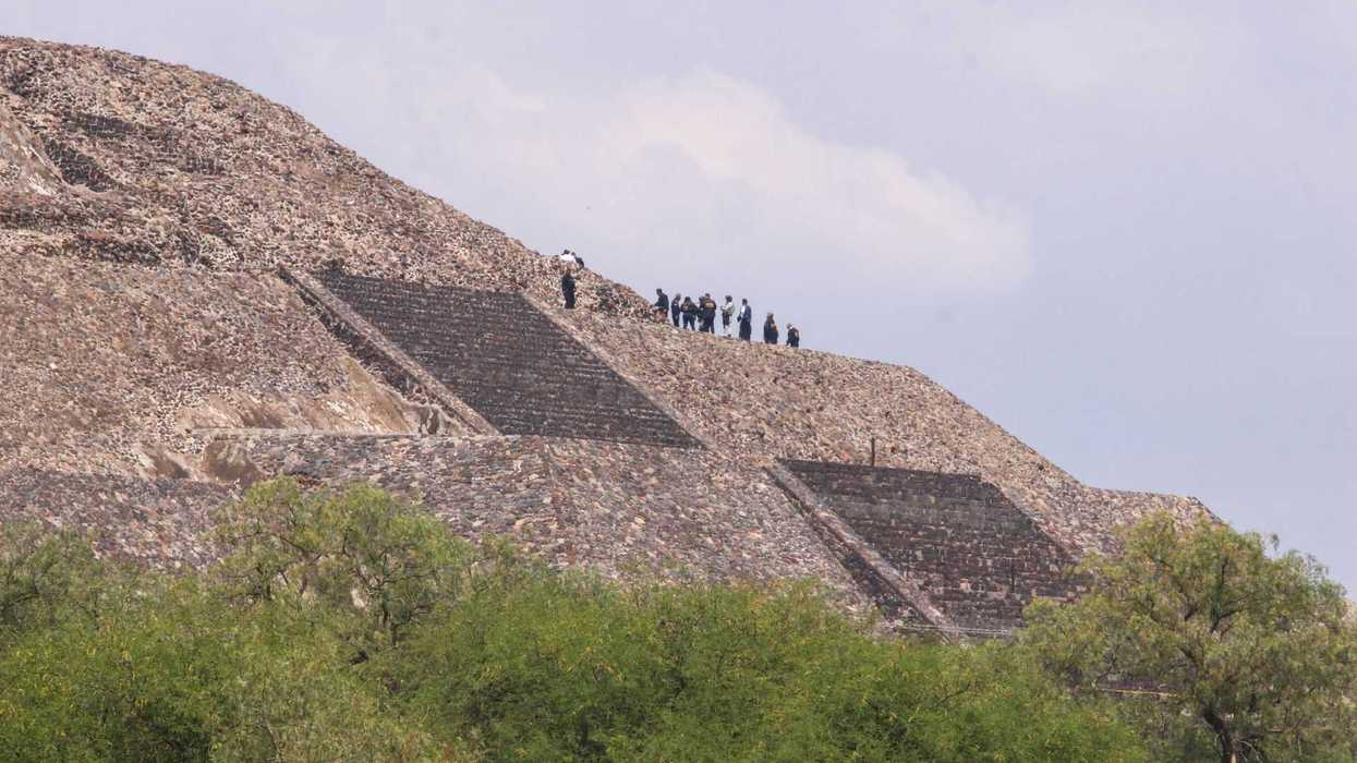 People standing atop the Pyramid of the Sun, Teotihuacan, with trees in the foreground.