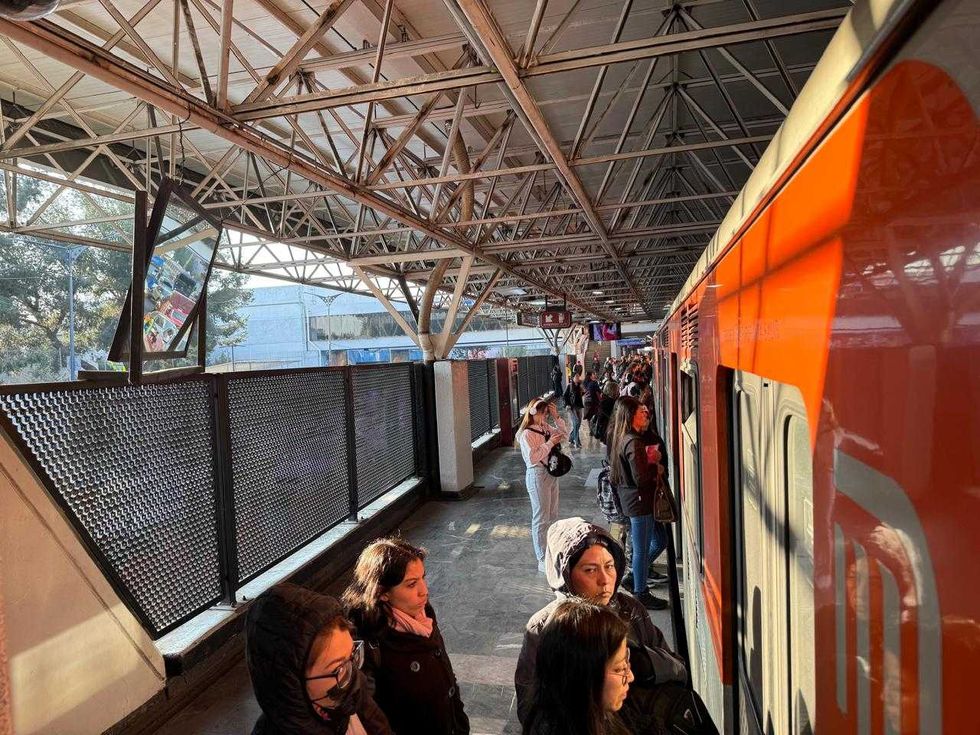 People waiting on a sunlit train platform beside an orange train.