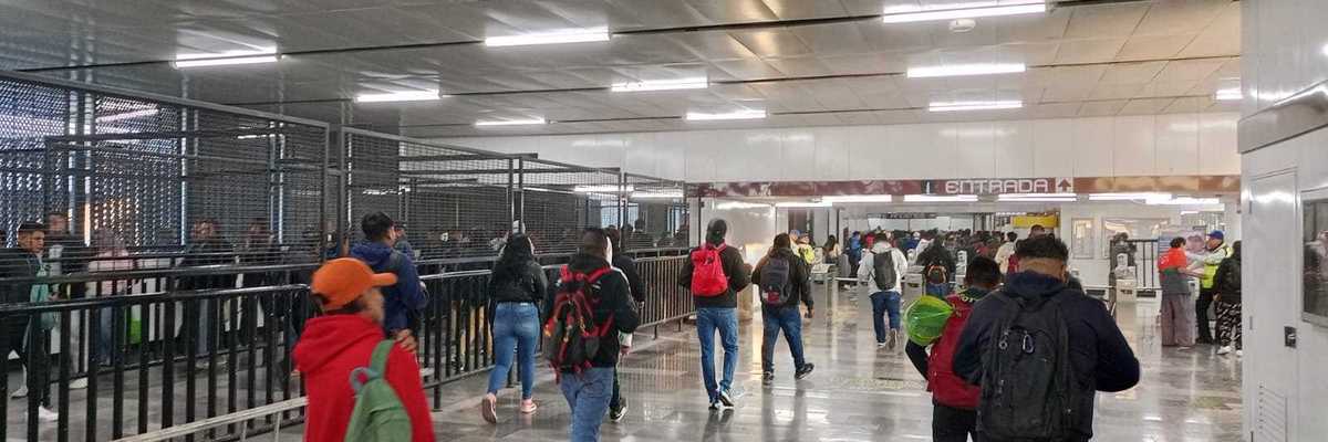 People walking in a busy subway station entrance with turnstiles and barriers.