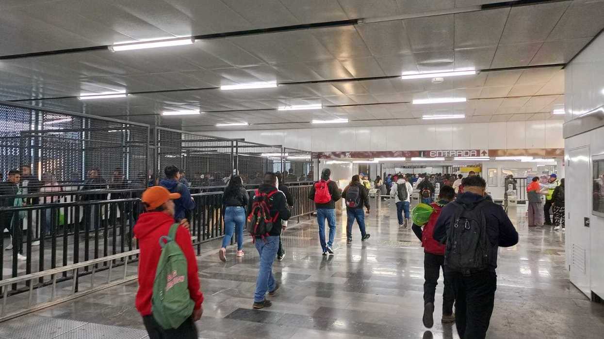 People walking in a busy subway station entrance with turnstiles and barriers.