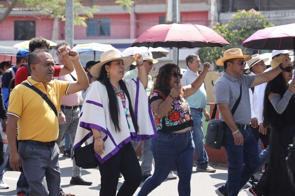 People walking in a protest, holding umbrellas, wearing hats, and raising fists.