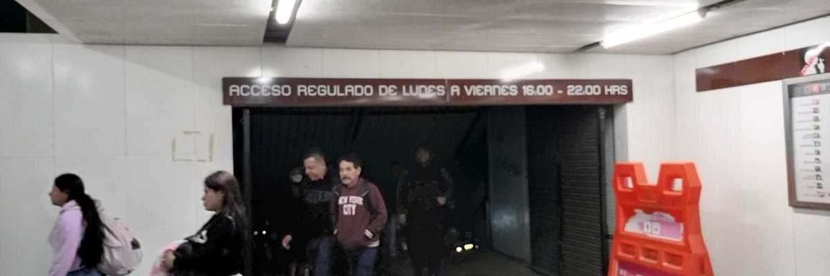 People walking in a subway corridor with a sign above and an orange barriers to the side.