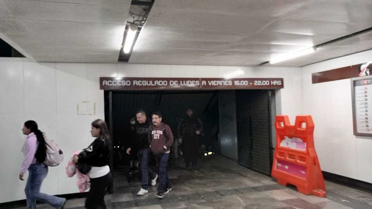 People walking in a subway corridor with a sign above and an orange barriers to the side.