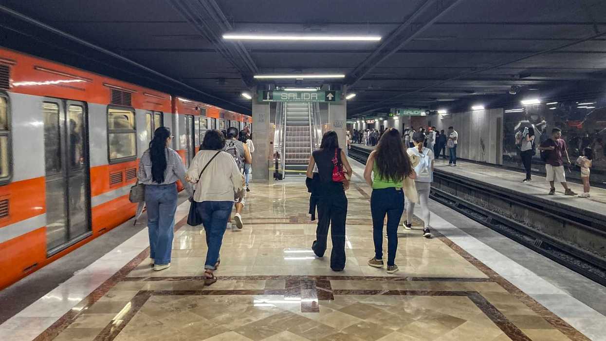 People walking in a subway station with an orange train on the left.