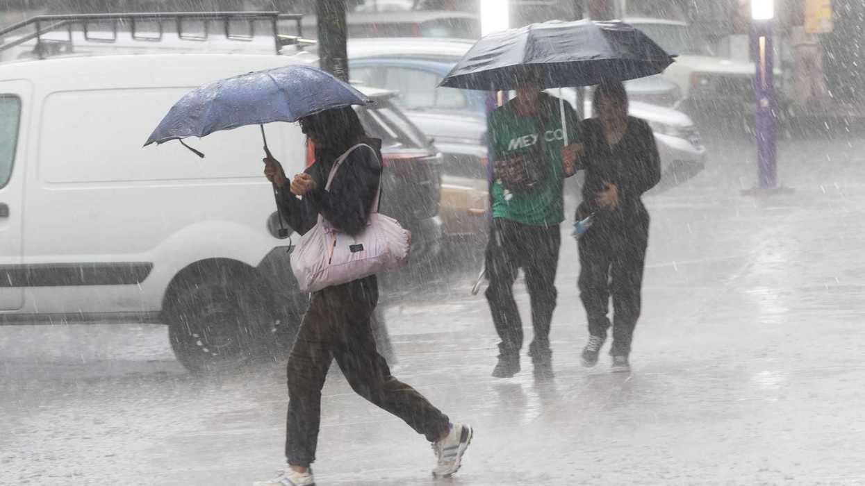 People walking with umbrellas in heavy rain on a city street.