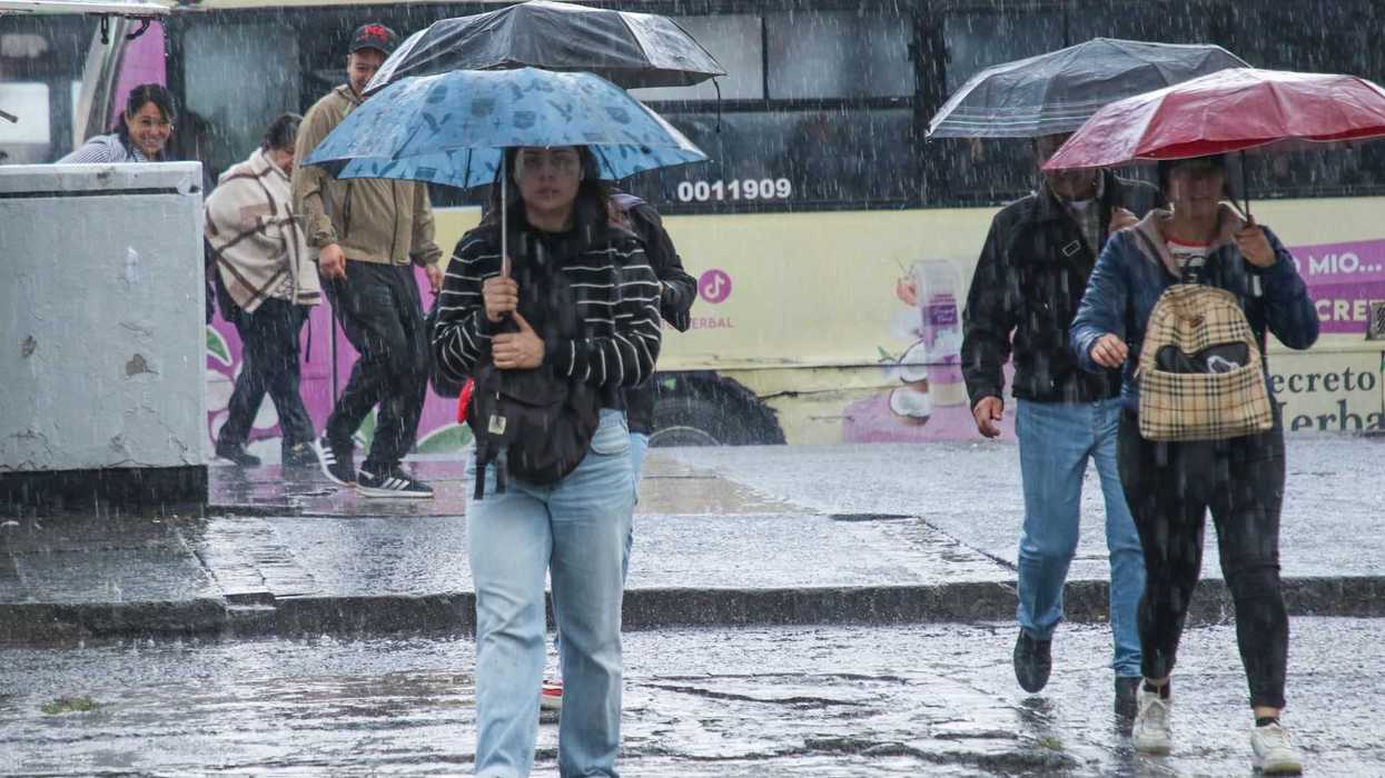 People with umbrellas walking in heavy rain near a bus.