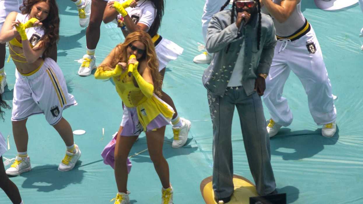 Performers singing and dancing energetically on stage with backup dancers in athletic outfits.