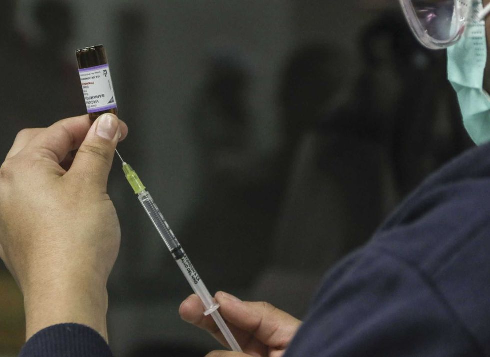 Person drawing liquid from a vial with a syringe.