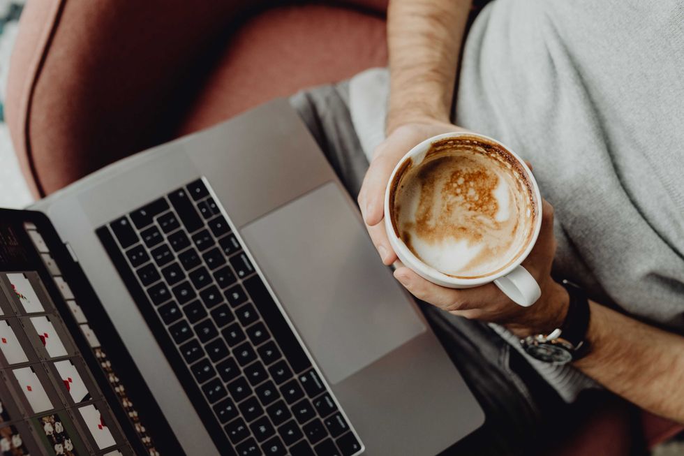 Person holding a cappuccino near a laptop.