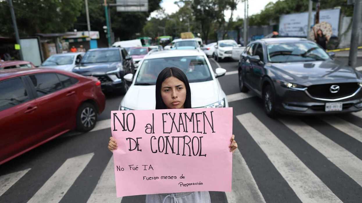 Person holding a protest sign on a crosswalk, with cars stopped behind them.
