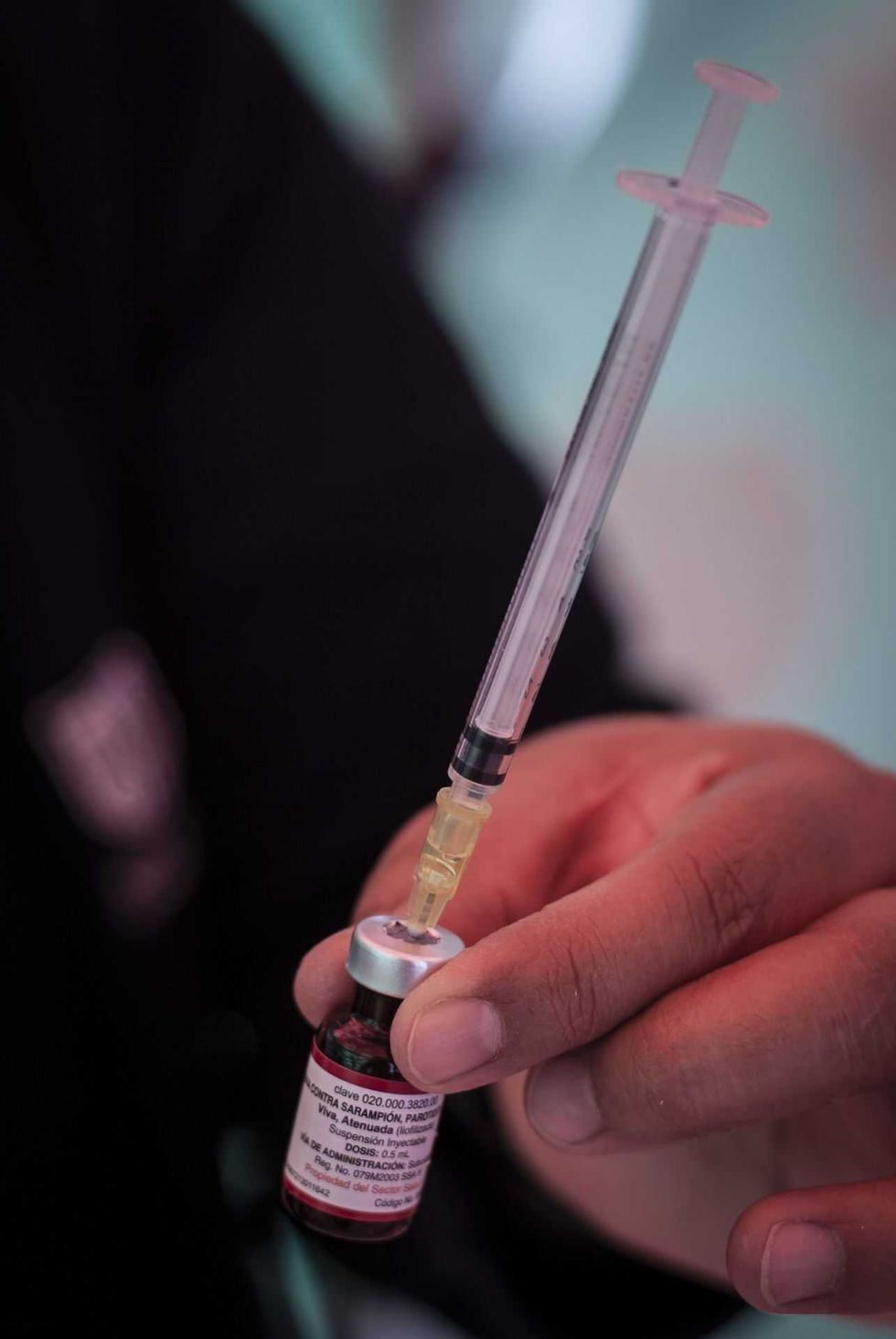 Person holding a syringe, drawing liquid from a vial.
