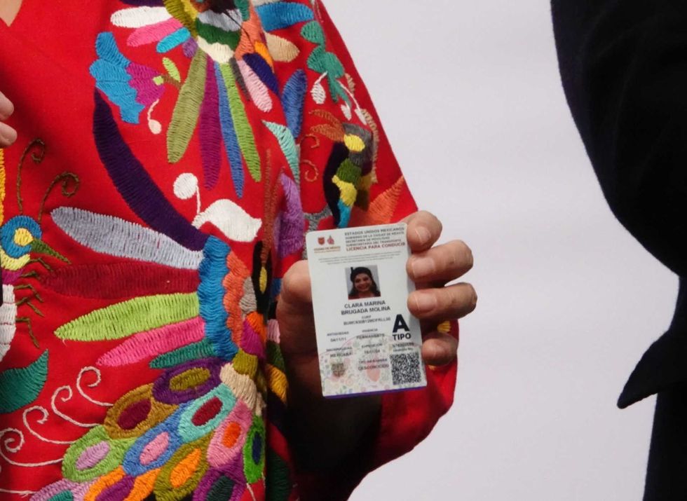Person holding an ID card, wearing colorful embroidered clothing.
