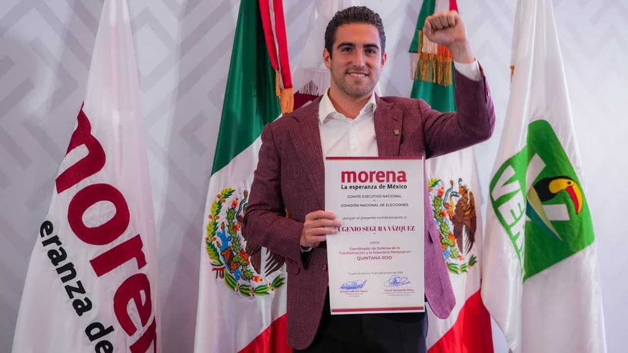 Person holding certificate, raising fist, standing by flags of Morena and Mexico.