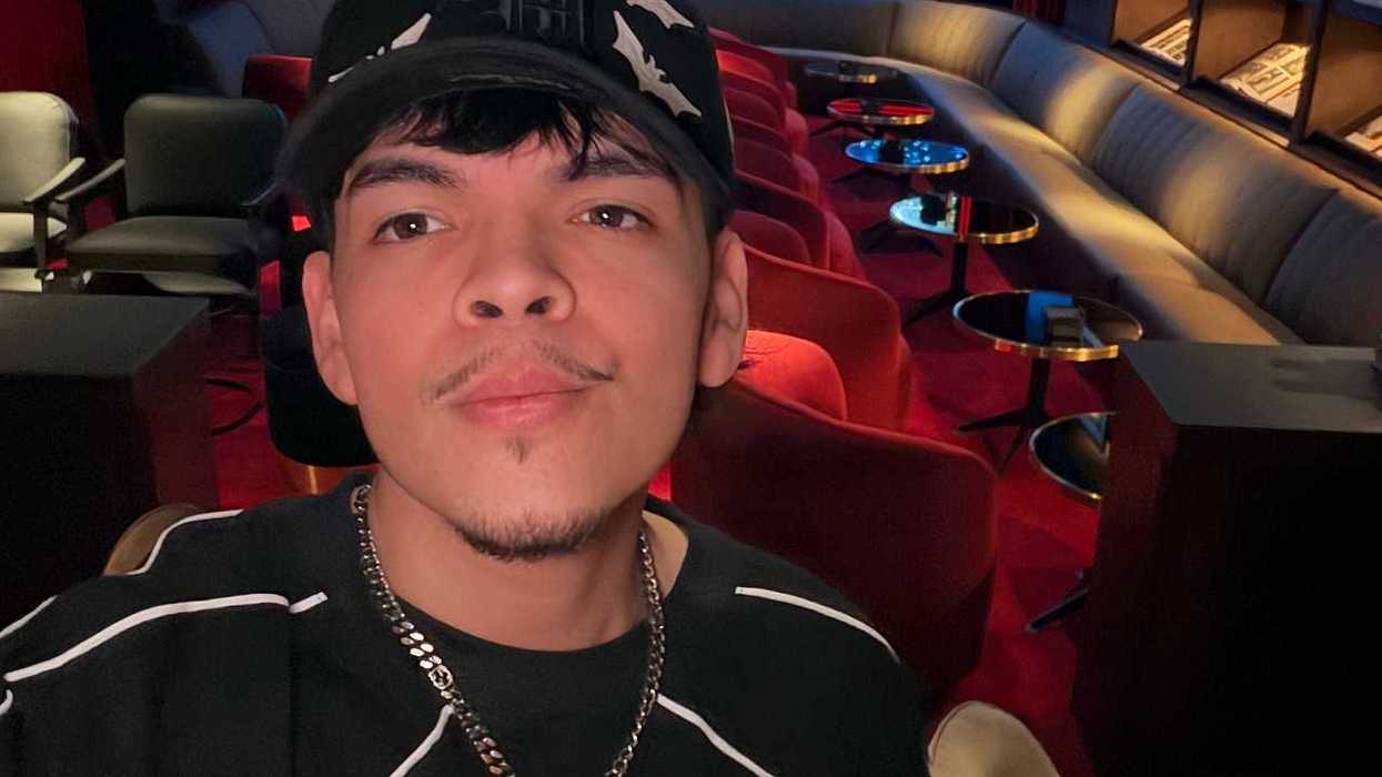Person in a cap takes a selfie in a cozy theater lounge with red seats and round tables.
