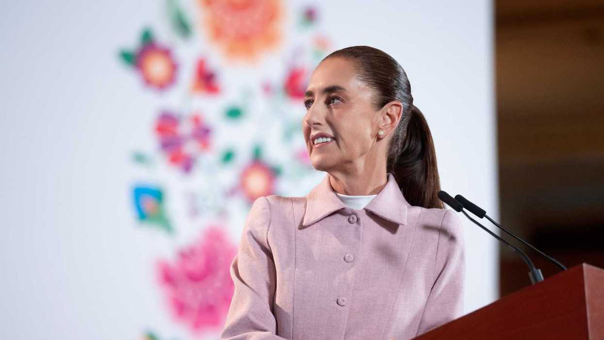 Person in a pink outfit speaking at a podium with floral backdrop.