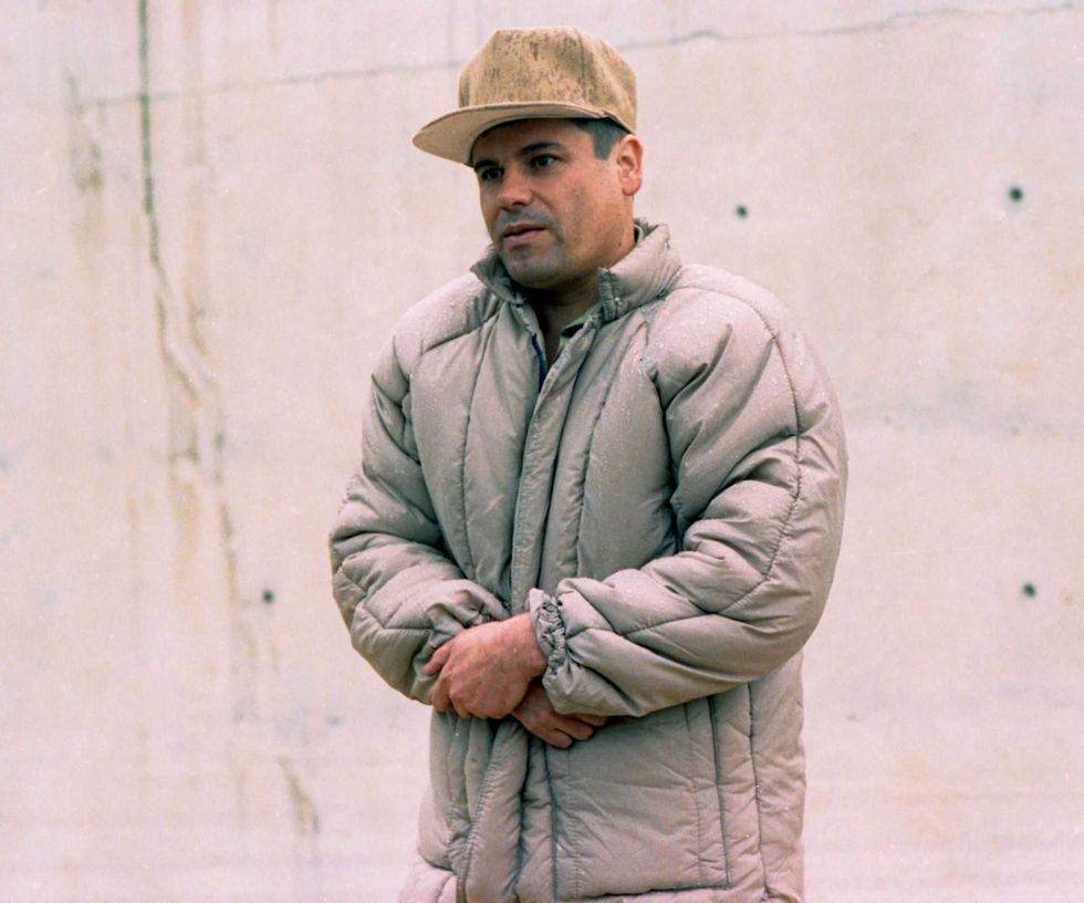 Person in a puffy jacket and cap stands against a concrete wall.