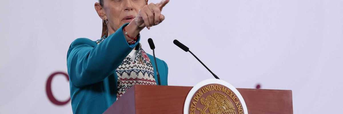 Person in a teal jacket speaks standing at a podium with a Mexican emblem.