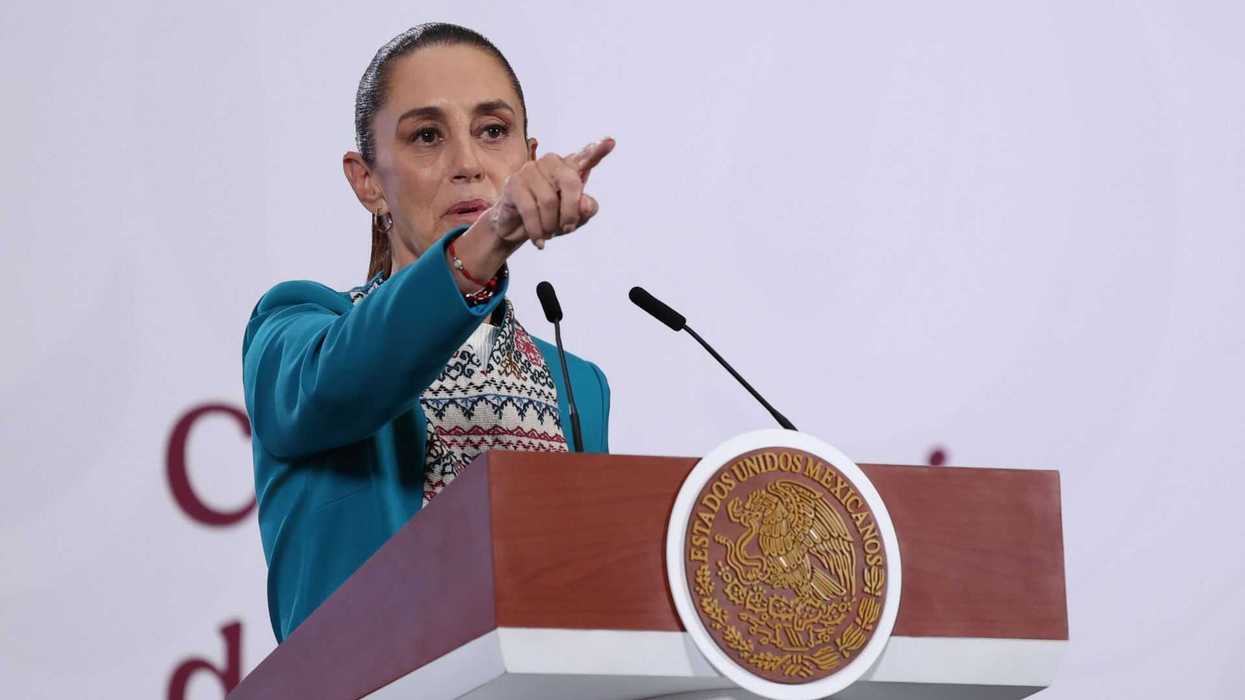Person in a teal jacket speaks standing at a podium with a Mexican emblem.