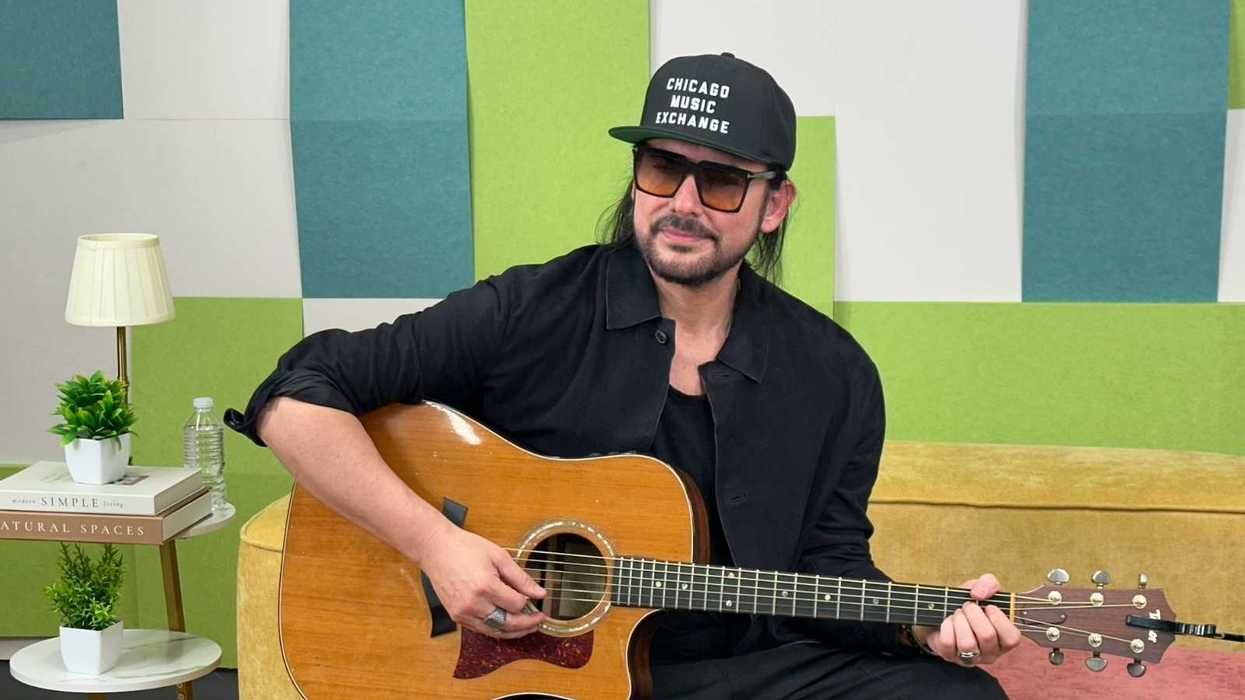 Person in black attire playing an acoustic guitar on a colorful couch.