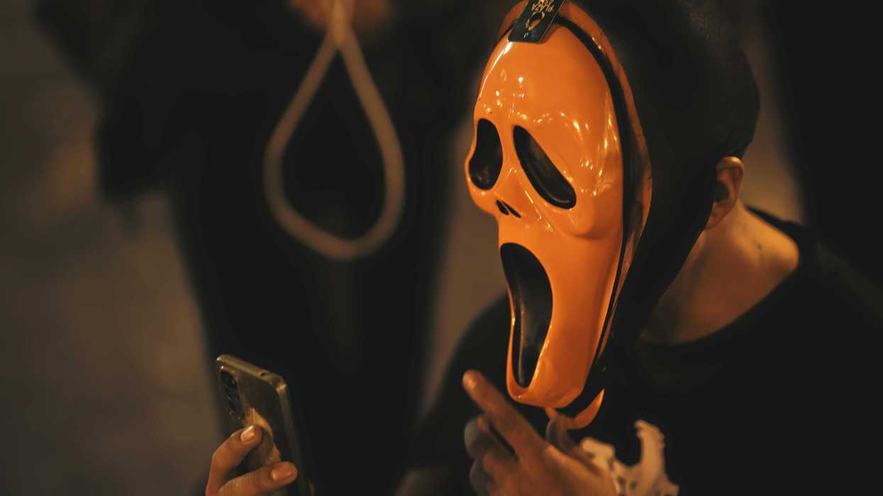 Person in orange scream mask looking at phone in dim lighting.