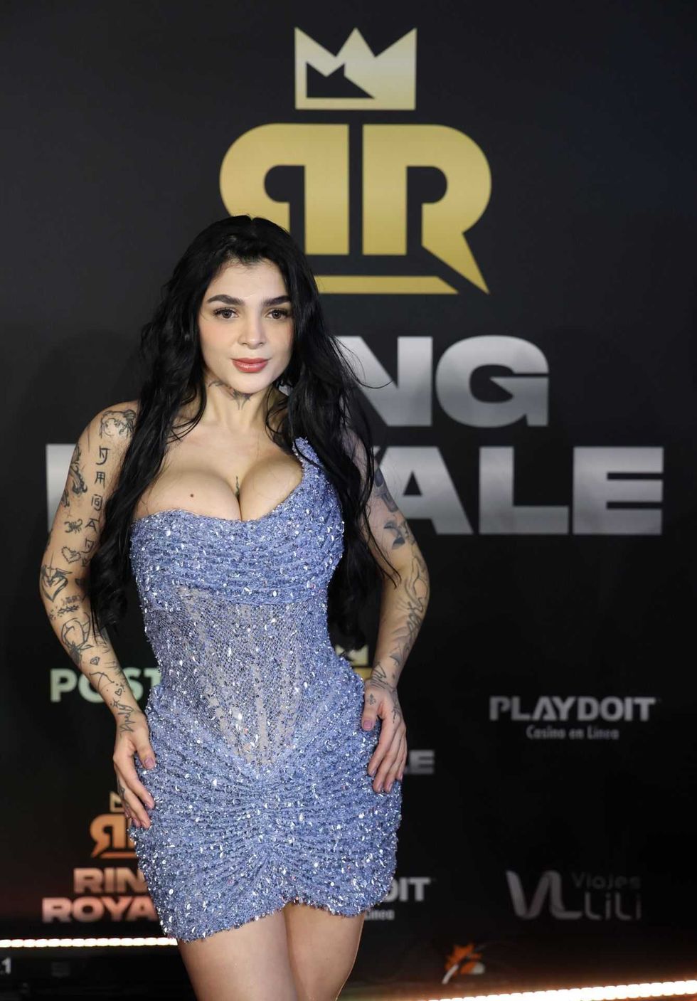 Person in sparkling dress with tattoos on arms at a red carpet event.