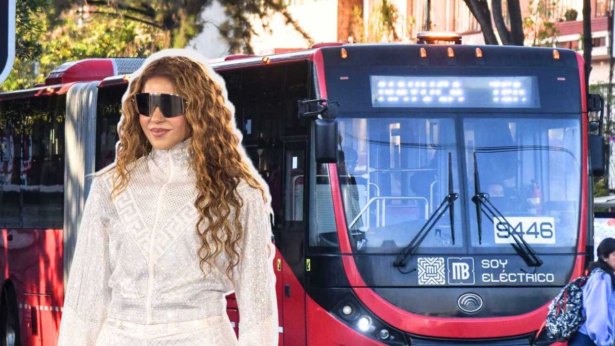 Person in sunglasses and white outfit in front of a red electric bus.
