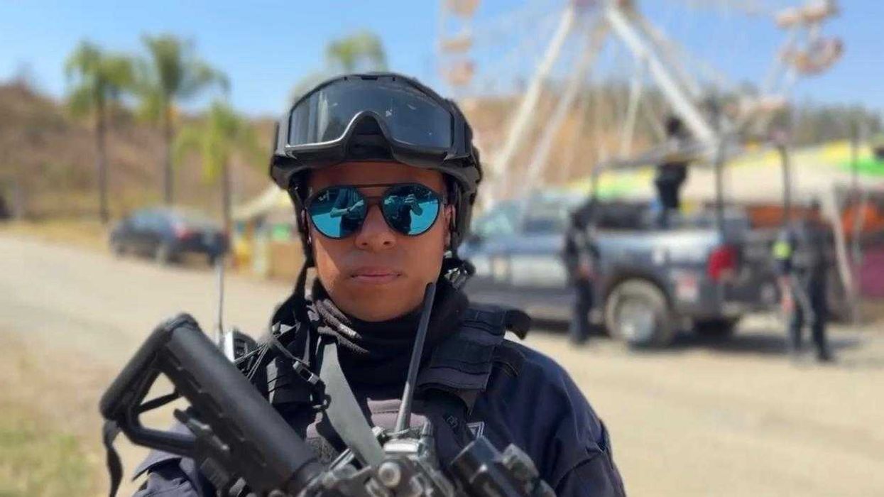 Person in tactical gear with a rifle, Ferris wheel in background, outdoors scene.