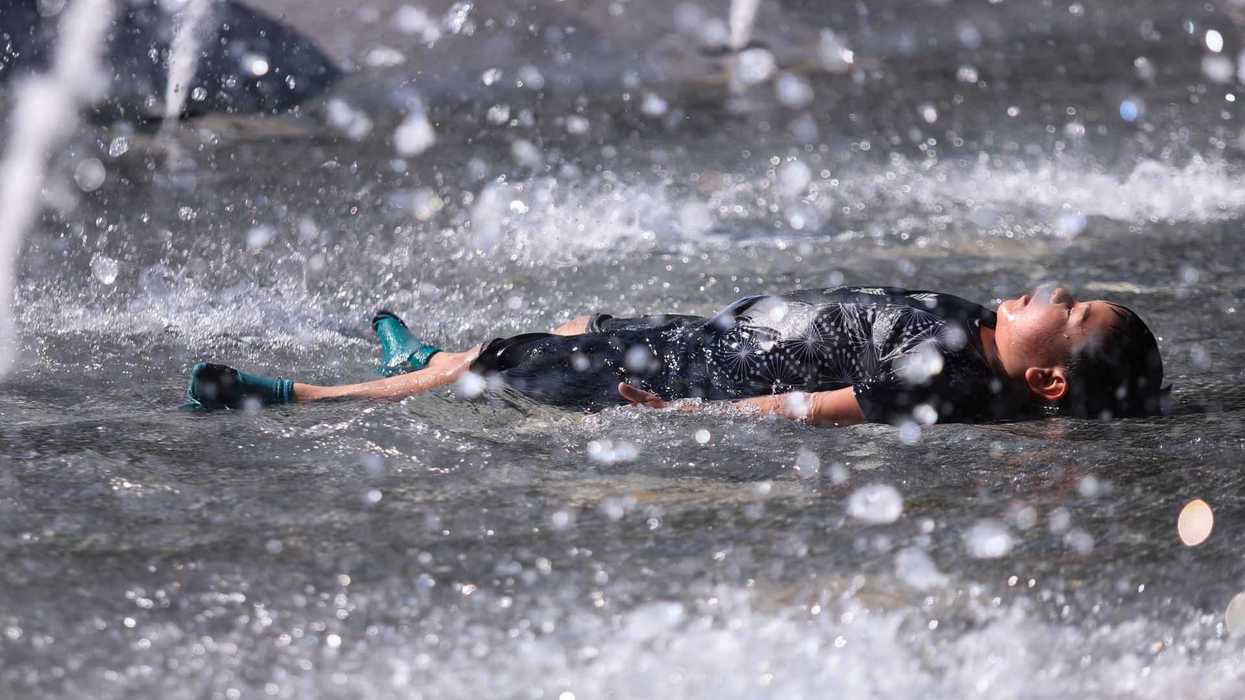 Person in wetsuit lying in a fountain with water spraying around.