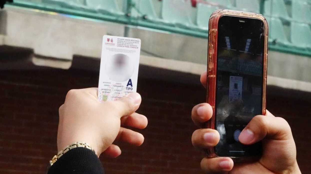 Person photographs a card with a smartphone indoors, in front of a blurred background.