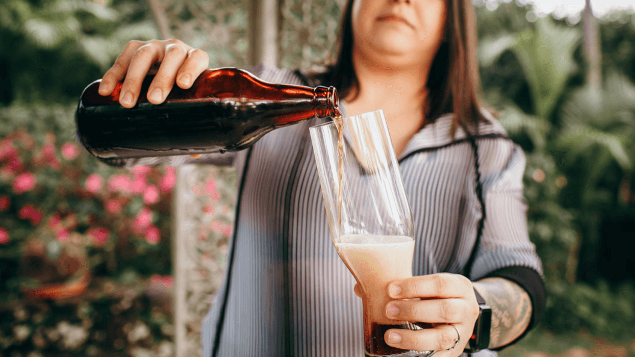 Person pouring beer from a bottle into a glass outdoors.