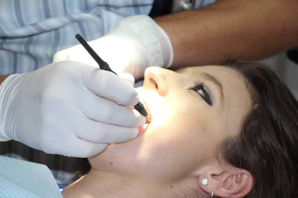 Person receiving dental examination with a gloved hand and dental tool in mouth.