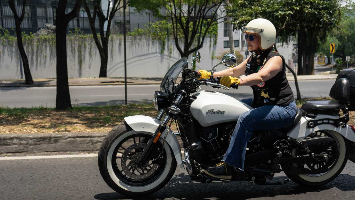 Person riding a white motorcycle on a tree-lined street.