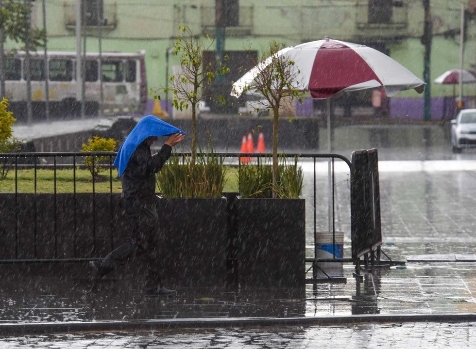 Person shields with blue cloth from heavy rain near an overturned umbrella.