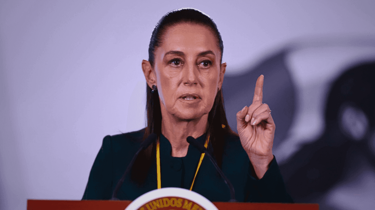Person speaking at a podium, gesturing with one finger raised.