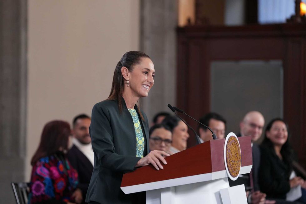 Person speaking at a podium with audience in the background, smiling.