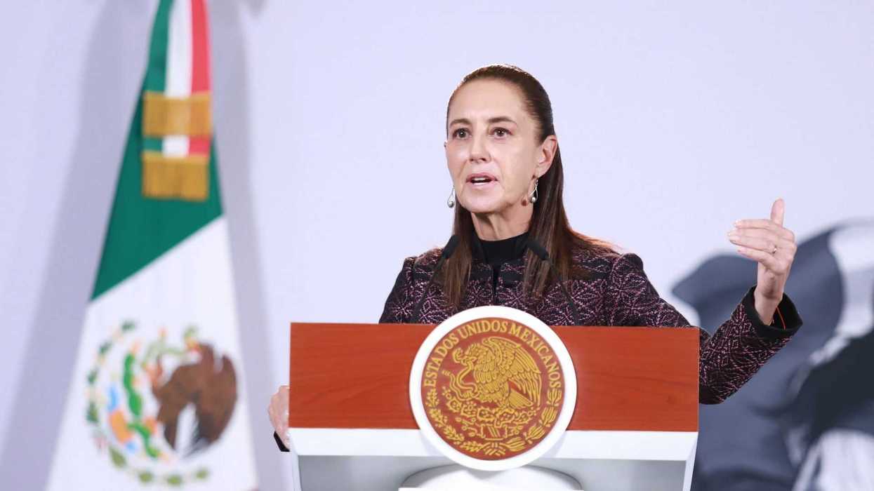 Person speaking at a podium with Mexican emblem, flag in background.